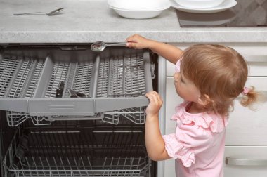 Sevimli sarışın bebek mutfakta yardım ediyor bulaşık makinesinden tabakları çıkarıyor. Çocuk ev işlerine yardım ediyor.