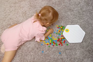 Güzel motor beceriler geliştiren masa oyunları. Çocuk halının üzerinde yatar ve çok renkli plastik parçalardan bir yapboz toplar.