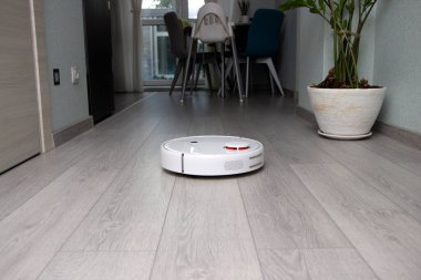 Robot elektrik süpürgesi daireyi temizliyor. Beyaz robot elektrik süpürgesi iç mekanda çalışıyor