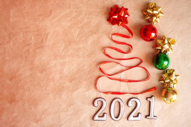 Kırmızı saten kurdele ve yıldızdan yapılmış güzel noel ağacı ve fotokopi alanı olan kahverengi arka planda 2021.