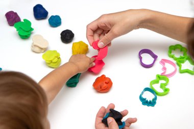 Beyaz bir masanın üzerinde renkli plastikçiden bebek heykelleri. Küçük bir çocuğun eli renkli plastiğin parçalarını sıkıyor. Anne kızıyla eğitim oyunları oynuyor.