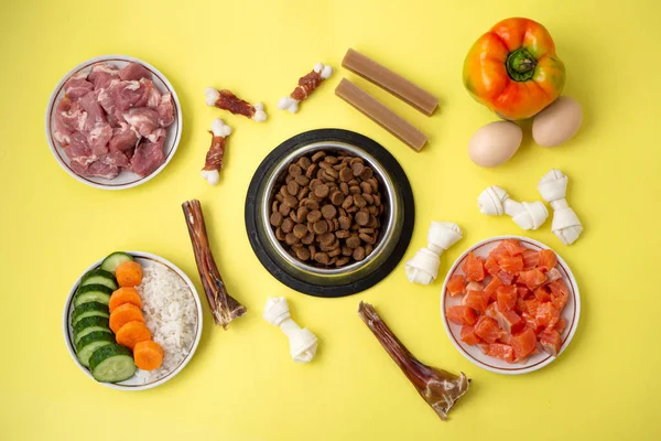 Dry pet dog food in bowl with natural ingredients and treats. Raw meat, fish, vegetables, eggs. concept of correct balanced and healthy nutrition menu for pet, flat lay