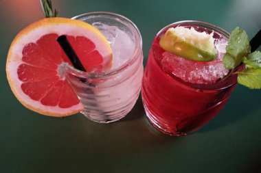 Aperatif zaman. iki serin, susuzluk-su verme kadeh alkollü içecekler nane, greyfurt dilim ve siyah plastik çöp ile süslenmiş. koyu kahverengi zemin