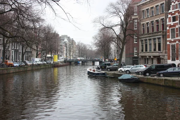 Escena de primavera temprana en la ciudad de Amsterdam. Tours en barco por los famosos canales holandeses. Paisaje urbano con casas de canal en Holanda, Países Bajos — Foto de Stock