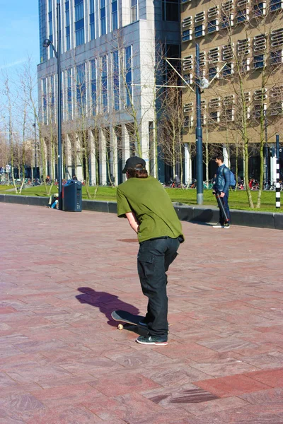 Pouliční chlapec vyrůstal v moderní metropoli Rotterdamu v Nizozemsku. Mladý muž trénací skateboard na náměstí mezi mrakodrapy a budovami — Stock fotografie