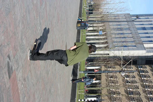 Menino de rua criado na metrópole moderna de Roterdão, na Holanda. Jovem pratica seu skate em uma praça entre os arranha-céus e edifícios — Fotografia de Stock
