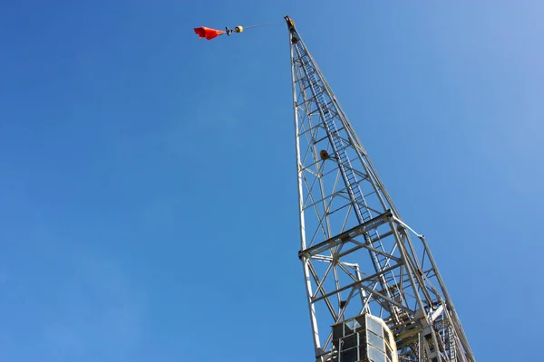 Lešení pylonů. vysoce industriální kovová konstrukce, na které je vyvěšena neznámá červená vlajka. obloha je světle modrá — Stock fotografie