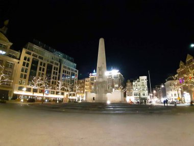 Amsterdam 'daki baraj meydanında gece vakti, Hollanda' da aydınlık sokaklar ve binalar var.