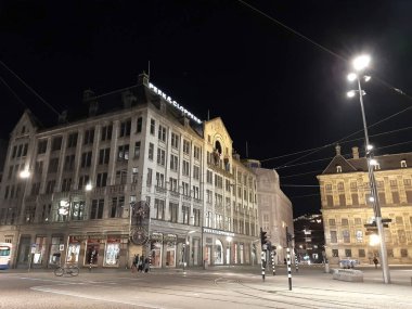 Amsterdam 'daki baraj meydanında gece vakti, Hollanda' da aydınlık sokaklar ve binalar var.