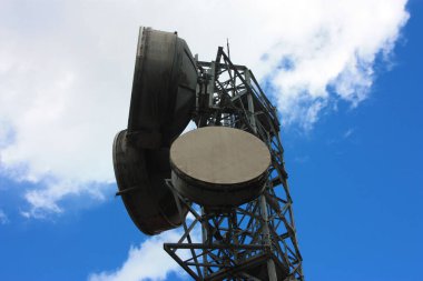 Şu anki uydu antenleri, yüksek yoğunluklu elektrik kabloları ve bulutlu mavi gökyüzü ile sinyal gönderen yüksek büyüklükteki antenler.