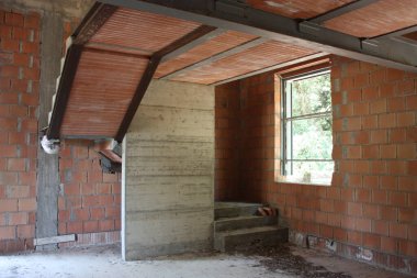 Tamamlanmamış, penceresi olan bir evde, kırmızı tuğla bina ve kirişler için inşaat çalışmaları devam ediyor.