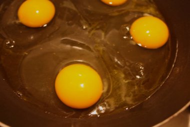 dört tavuk yumurtası siyah bir tavada pişiriliyor.