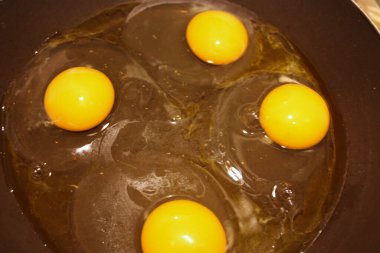 dört tavuk yumurtası siyah bir tavada pişiriliyor.