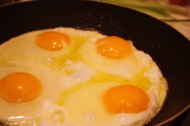 dört tavuk yumurtası siyah bir tavada pişiriliyor.