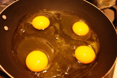 dört tavuk yumurtası siyah bir tavada pişiriliyor.