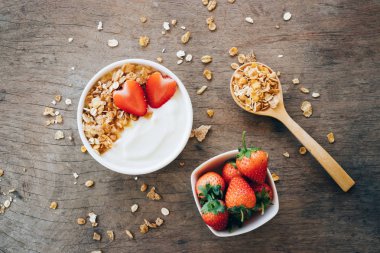 Beyaz ahşap masa üzerinde üstten görünüm yoğurt bir granola ile ahşap kase, taze çilek. Sağlık gıda kavramı.
