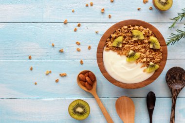 Mavi ahşap masa üzerinde üstten görünüm granola, taze kivi, nane ve kaşık ahşap bir kase yoğurt. Sağlık gıda kavramı.