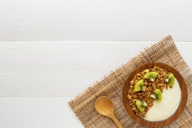 Mavi ahşap masa üzerinde üstten görünüm granola, taze kivi, nane, badem ve kaşık ahşap bir kase yoğurt. Sağlık gıda kavramı.