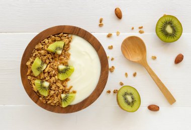 Mavi ahşap masa üzerinde üstten görünüm granola, taze kivi, nane, badem ve kaşık ahşap bir kase yoğurt. Sağlık gıda kavramı.
