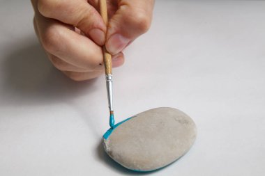 Handmade - stone painting. production decoration. Female hand are drawing  on the stone. Horizontally. clipart