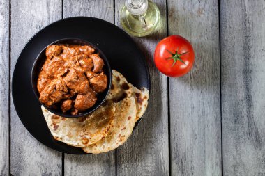 Chicken tikka masala served with bread naan in black dish. Top view clipart