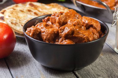 Chicken tikka masala served with bread naan in black dish clipart