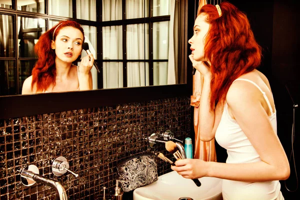 若い女性が化粧を適用します 赤い髪の少女 鏡で見ていると大きなブラシで化粧品を適用します — ストック写真
