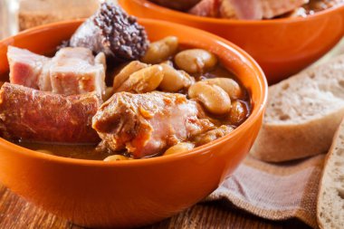 Bowl with fabada asturiana. Traditional spanish bean stew with chorizo, bacon and other meats clipart