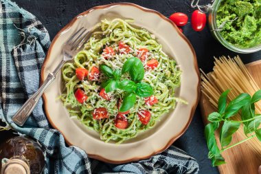 Vegetarian pasta spaghetti with basil pesto and cherry tomatoes. Italian dish. Top view clipart