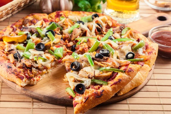 Pizza with chicken gyros, green pepper, olives and onion on cutting board. Served with beer