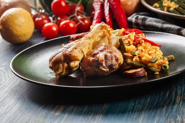 Traditionele paella met kip benen, worst chorizo en groenten geserveerd op de zwarte plaat — Stockfoto