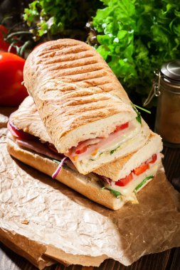 Toasted panini with ham, cheese and arugula sandwich on a paper clipart