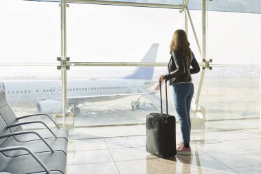 Dikiz atış havaalanındaki bagaj ile ayakta ve camdan arayan bir kadın.