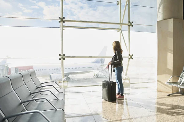 woman standing with luggage at the airport and looking through the glass window.