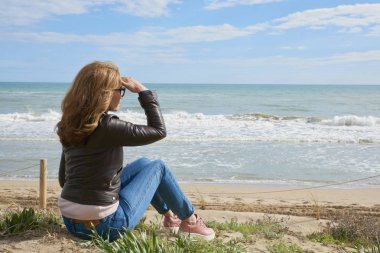 Arka görünümü atış vasıl belgili tanımlık kıyı oturan ve uzağa arıyorsunuz rahat orta yaşlı kadın.