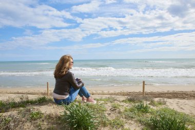 Arka görünümü atış vasıl belgili tanımlık kıyı oturan ve uzağa arıyorsunuz rahat orta yaşlı kadın.