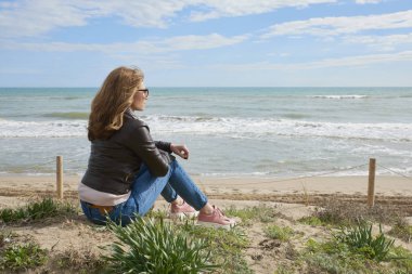Arka görünümü atış vasıl belgili tanımlık kıyı oturan ve uzağa arıyorsunuz rahat orta yaşlı kadın.