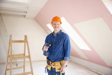 Kendine güvenen orta yaşlı tamirci el matkap duran inşaat alanında tutarak. 