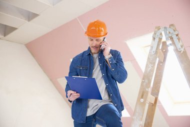Cep telefonunu kullanarak ve merdiven, dururken biriyle danışmanlık inşaat işçisi portresi.