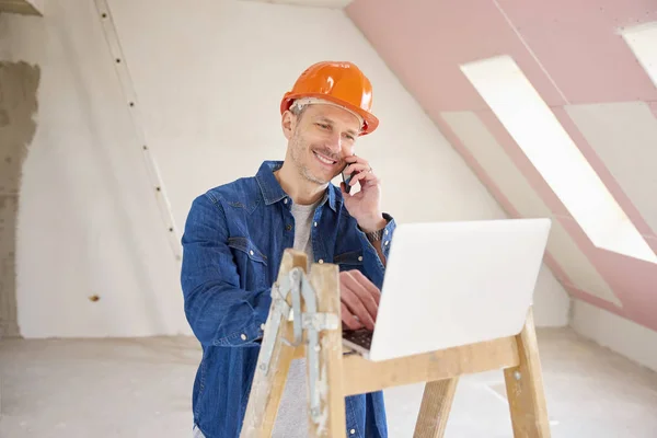 建筑地盘使用手提电脑时 使用手提电话及咨询他人的快乐建筑工人肖像 — 图库照片
