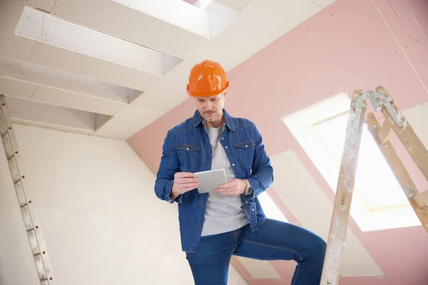 建設現場で梯子の上に立っている間デジタル タブレットを使用して中間の老化させた建設労働者の肖像画 — ストック写真