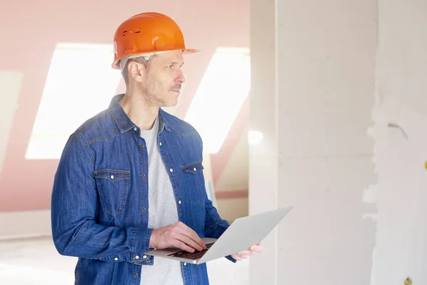 中年建筑工人手持笔记本电脑在他的手 而当站在建设工地和工作 — 图库照片