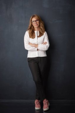 Çekici olgun işkadını karşı kameraya bakıyor ve gülümsüyor koyu arka plan ayakta, tam uzunlukta vurdu. 