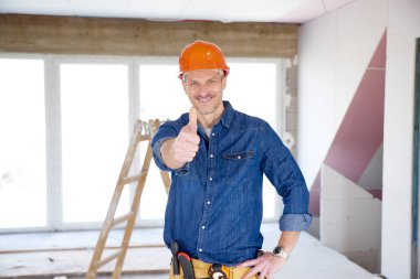 Kask ve gösteren başparmak yukarı kameraya bakarak ve gülümseyen giyen gülümseyen el ulağı portresi. 