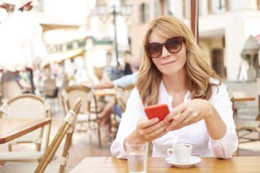 Onun cep telefonu ve kafede otururken mesajlaşma metin kullanarak gülümseyen çekici kadın portresi.