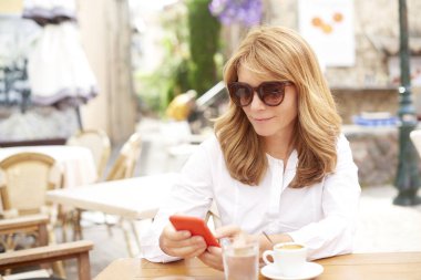 Onun cep telefonu ve kafede otururken mesajlaşma metin kullanarak gülümseyen çekici kadın portresi.