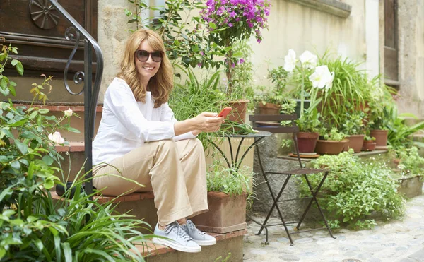 Onun cep telefonu ve açık ve rahatlatıcı otururken mesajlaşma metin kullanarak çekici gülümseyen kadın portresi. 