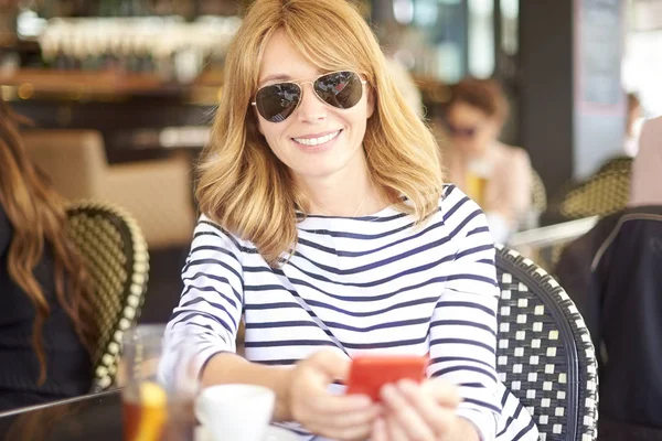 一个快乐成熟的女人的肖像使用她的手机和短信 而坐在咖啡馆户外 — 图库照片