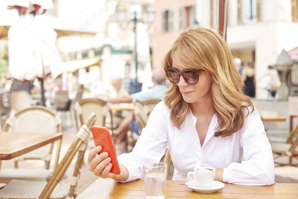 Portrait of smiling attractive woman using her mobile phone and text messaging while sitting at cafe.