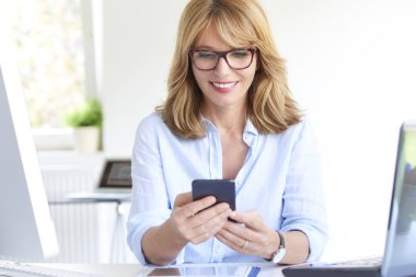 Güzel iş kadını kısa süre ofis masası oturma ve çalışma dizüstü bilgisayar ve bilgisayar mesaj. Çoklu görev. 